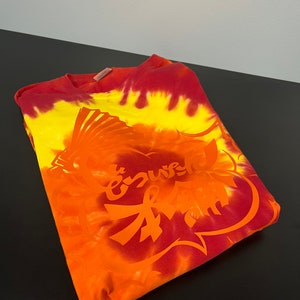 May include: A tie-dye t-shirt with a red, orange, and yellow color scheme. The shirt features a large, red graphic of a heart with the word "enuf" written inside.