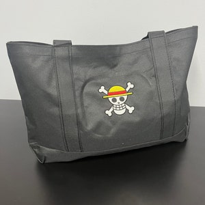 May include: Black tote bag with a white skull and crossbones design. The skull is wearing a yellow and red straw hat.