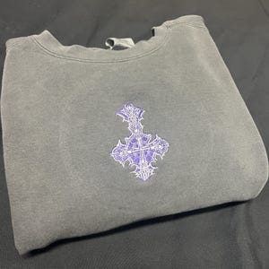 May include: A gray sweatshirt with a purple embroidered cross design.