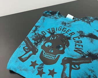 May include: A blue tie-dye t-shirt with a black skull and crossbones design. The text "Bad Trigger Crew" is printed around the skull.