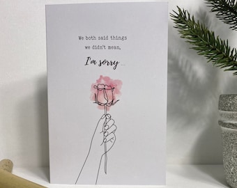 May include: A white card with a black line drawing of a hand holding a pink watercolor rose. The card reads "We both said things we didn't mean. I'm sorry..."
