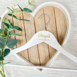 Op de afbeelding: Witte houten hanger met de naam "Abigail Bridesmaid" in gouden letters.