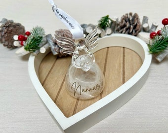 May include: A clear glass angel ornament with feathery filling, resting in a white heart-shaped wooden tray. The angel has silver wings and a ribbon that reads "in angels are near". The ornament is personalized with the name "Nannar".