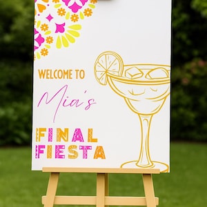 May include: A white sign on a wooden easel with the text "WELCOME TO Mia's FINAL FIESTA". The sign has a margarita illustration and floral designs in yellow, pink, and orange.