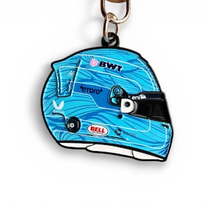 May include: A light blue racing helmet keychain with a black outline. The helmet features a wave pattern and logos for BWT, etoro, and Bell. The visor is black. A metal ring is attached to the top.