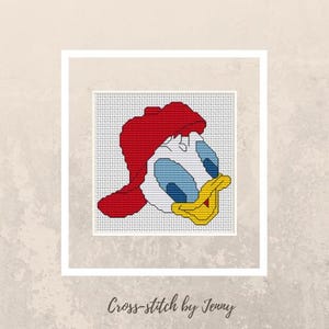 Könnte beinhalten: Kreuzstich-Kunst mit einer Cartoon-Ente mit roter Mütze, blauen Augen und gelbem Schnabel. Das Kunstwerk ist in einem weißen Rahmen eingefasst und vor einem neutralen Hintergrund platziert. Der Text "Cross-stitch by Jenny" steht unten.