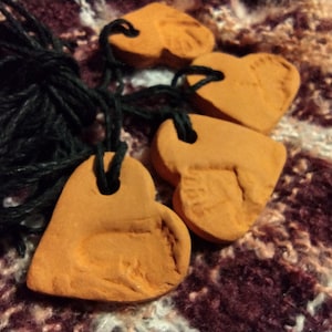 Puede incluir: Cuatro adornos de corazón de terracota con una cuerda atada a cada uno. Los corazones tienen un diseño en relieve en la parte delantera.