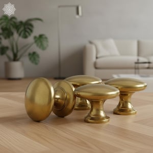 Peut inclure: Ensemble de boutons de porte et une poignée de porte dorés. Les boutons ont une forme arrondie en forme de champignon, tandis que la poignée est ovale. La quincaillerie est présentée sur une surface en bois clair, suggérant un thème de décoration intérieure.