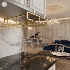 Puede incluir: Un estante de metal dorado para copas de vino instalado debajo de un armario, que sostiene varias copas de vino transparentes. La cocina cuenta con una encimera de mármol negro y una lámpara de araña.