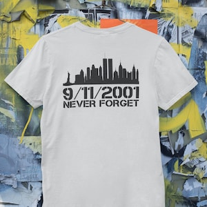 Könnte beinhalten: Weißes T-Shirt mit einer schwarzen Silhouette der New Yorker Skyline und dem Text "9/11/2001 NEVER FORGET".