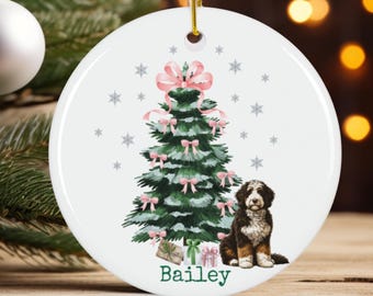 May include: A white, round Christmas ornament with a watercolor illustration of a decorated Christmas tree, a dog, and the name "Bailey". The tree has pink bows and is surrounded by snowflakes. The dog is black, brown, and white.