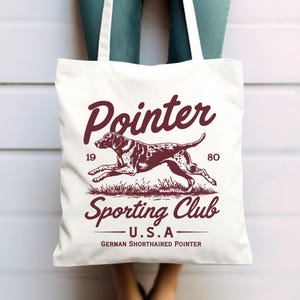 May include: White canvas tote bag with a brown graphic of a German Shorthaired Pointer running. The text "Pointer Sporting Club - U.S.A - German Shorthaired Pointer" is printed on the bag.