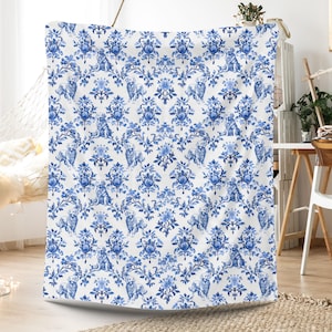 May include: A white and blue patterned blanket featuring a repeating design of dogs and floral elements. The pattern is in a classic damask style, with the dogs and flowers in a deep blue color against a white background.