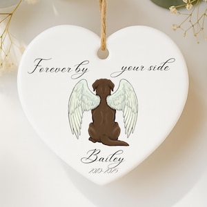 May include: White heart-shaped ornament with a brown dog illustration wearing angel wings. The text "Forever by your side" and the name "Bailey" with dates are printed on the ornament. A jute string is attached for hanging.