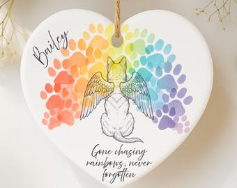 May include: Heart-shaped ceramic ornament with a pet memorial theme. Features a white cat with angel wings, rainbow paw prints, and the text "Gone chasing rainbows, never forgotten." Includes the name "Bailey" in script.