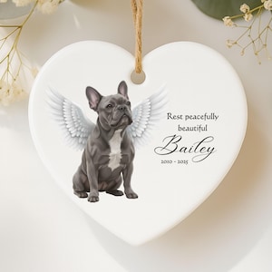 May include: Heart-shaped ceramic ornament featuring a gray French Bulldog with angel wings. The ornament includes the text "Rest peacefully beautiful Bailey 2010-2025" and a jute string for hanging.