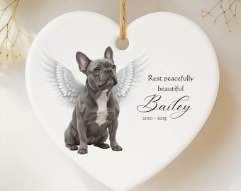 May include: Heart-shaped ceramic ornament featuring a gray French Bulldog with angel wings. The ornament includes the text "Rest peacefully beautiful Bailey 2010-2025" and a jute string for hanging.