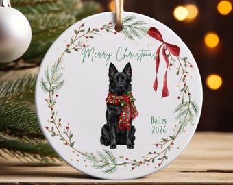 May include: A round white ceramic Christmas ornament featuring a black German Shepherd dog wearing a red and green plaid scarf. The ornament is decorated with a green pine wreath, a red ribbon, and the text Merry Christmas, Bailey, and 2026.