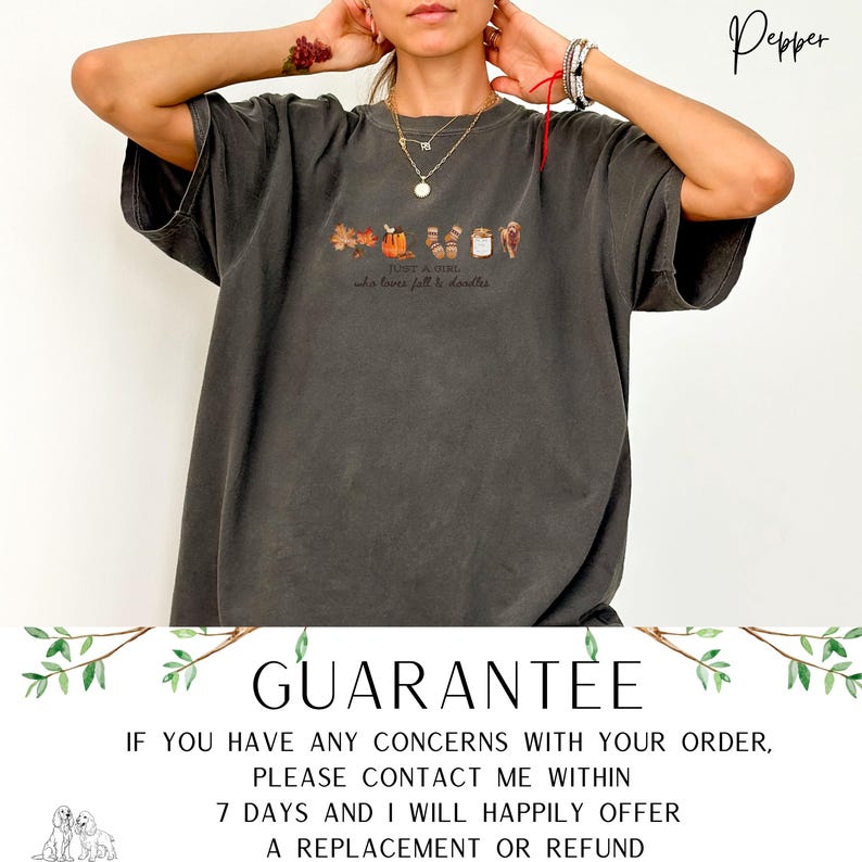 May include: Dark gray t-shirt with a fall-themed graphic. The graphic includes leaves, a pumpkin, a mug, and other autumn elements. Text on the shirt reads "JUST A GIRL who loves fall & doodles." The shirt has a relaxed fit.