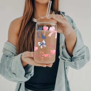 May include: A clear glass reusable water bottle with a bamboo lid and a glass straw. The bottle is decorated with pink hearts, blue bows, and a cartoon corgi dog. The text "xoxo" is printed on the bottle.