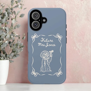 May include: A blue phone case with a white illustration of a dog holding a cocktail. The text "Future Mrs. Jones" is written in a decorative font within a white frame with bow accents. The case has a camera cutout.
