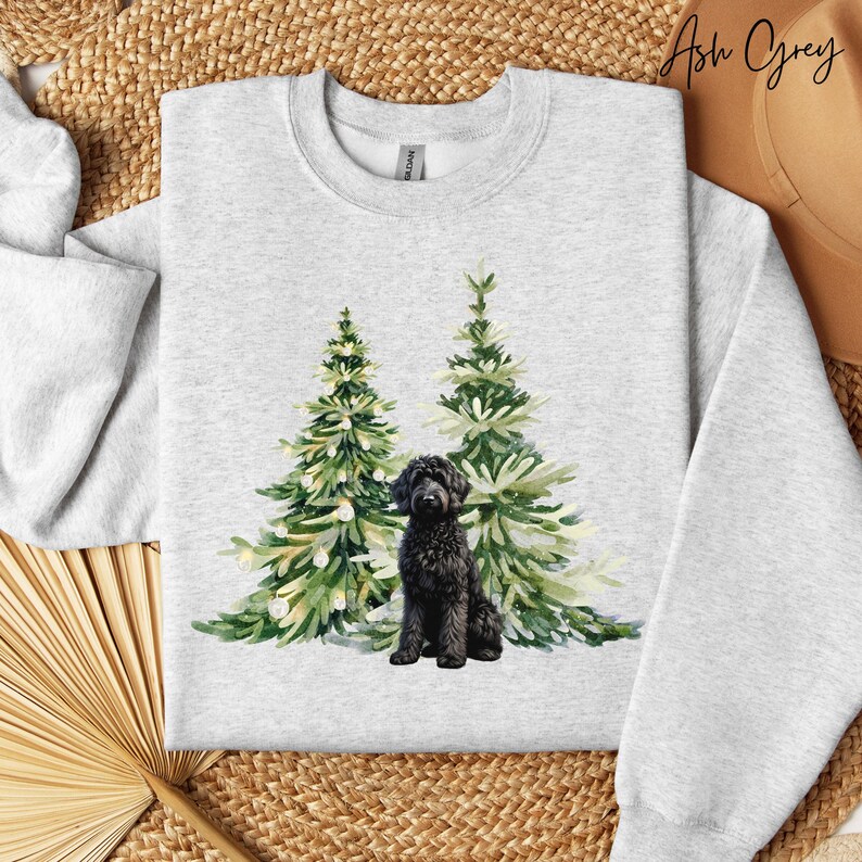 May include: Light grey Ash Grey sweatshirt with a watercolour design of two Christmas trees and a black dog. The dog sits in front of the trees. The sweatshirt is a crew neck.