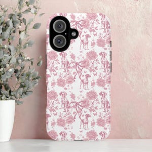 May include: A white phone case with a repeating pattern of pink roses, bows, butterflies, and dog illustrations. The case has a dual-lens camera cutout and black side buttons. The design is a toile-inspired print.