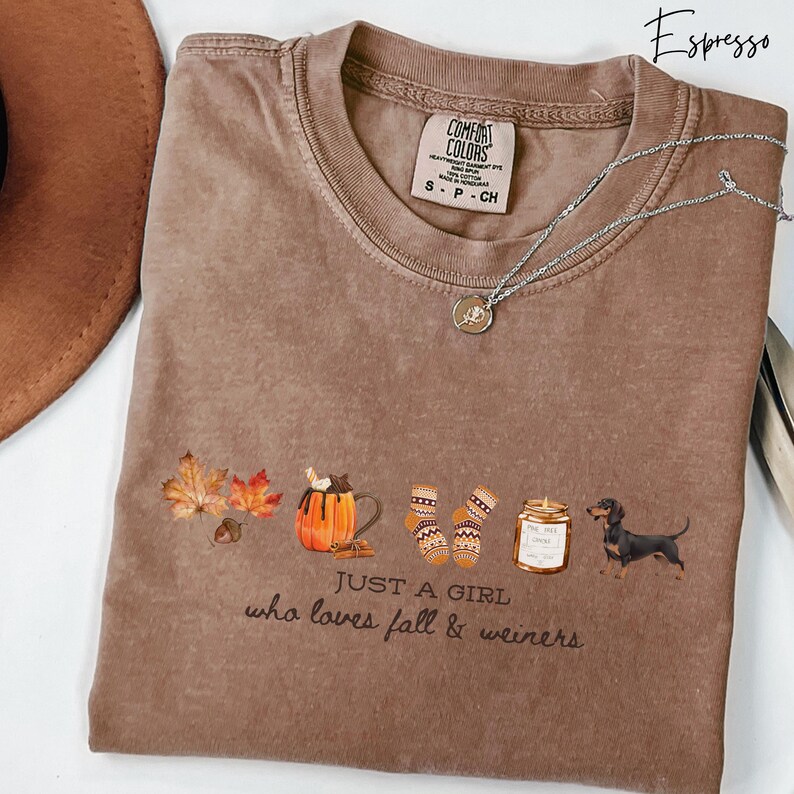 May include: Espresso-colored Comfort Colors t-shirt with a graphic design featuring fall leaves, a pumpkin spice latte, socks, a candle, and a dachshund. The text reads "Just a girl who loves fall & weiners."