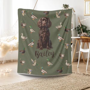May include: A green blanket featuring a brown dog with the name "Bailey" in cursive script. The blanket is decorated with illustrations of ducks in various poses. The dog is centered, with ducks scattered around the edges.