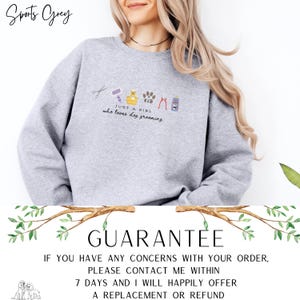 May include: A light grey sweatshirt featuring the embroidered text "JUST A GIRL who loves dog grooming" and dog grooming tools. The garment has a crew neck and long sleeves. The word "GUARANTEE" is printed below the sweatshirt.
