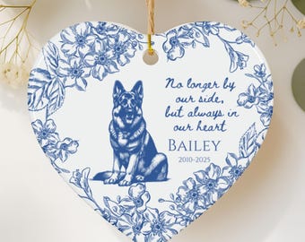 May include: Heart-shaped ceramic ornament with a blue floral border and a blue illustration of a German Shepherd. Text reads "No longer by our side, but always in our heart" and "BAILEY 2010-2025". Includes a jute twine for hanging.