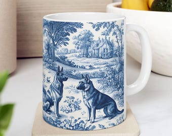 May include: A white ceramic mug with a blue and white design featuring two German Shepherd dogs in a pastoral setting. The design includes a house, trees, and flowers.