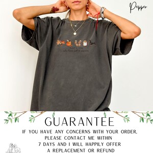 May include: Dark gray t-shirt with a fall-themed graphic. The design includes leaves, pumpkins, socks, and a dachshund, with the text "Just a girl who loves fall & weiners". The shirt has a relaxed fit.