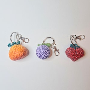 May include: Three keychains featuring different coloured heart-shaped charms with a swirl pattern. The charms are orange, purple and red.