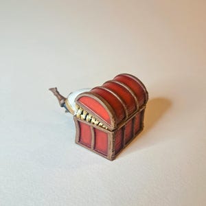 May include: A red wooden treasure chest with gold accents and a hinged lid. The chest is open and the lid is propped up.