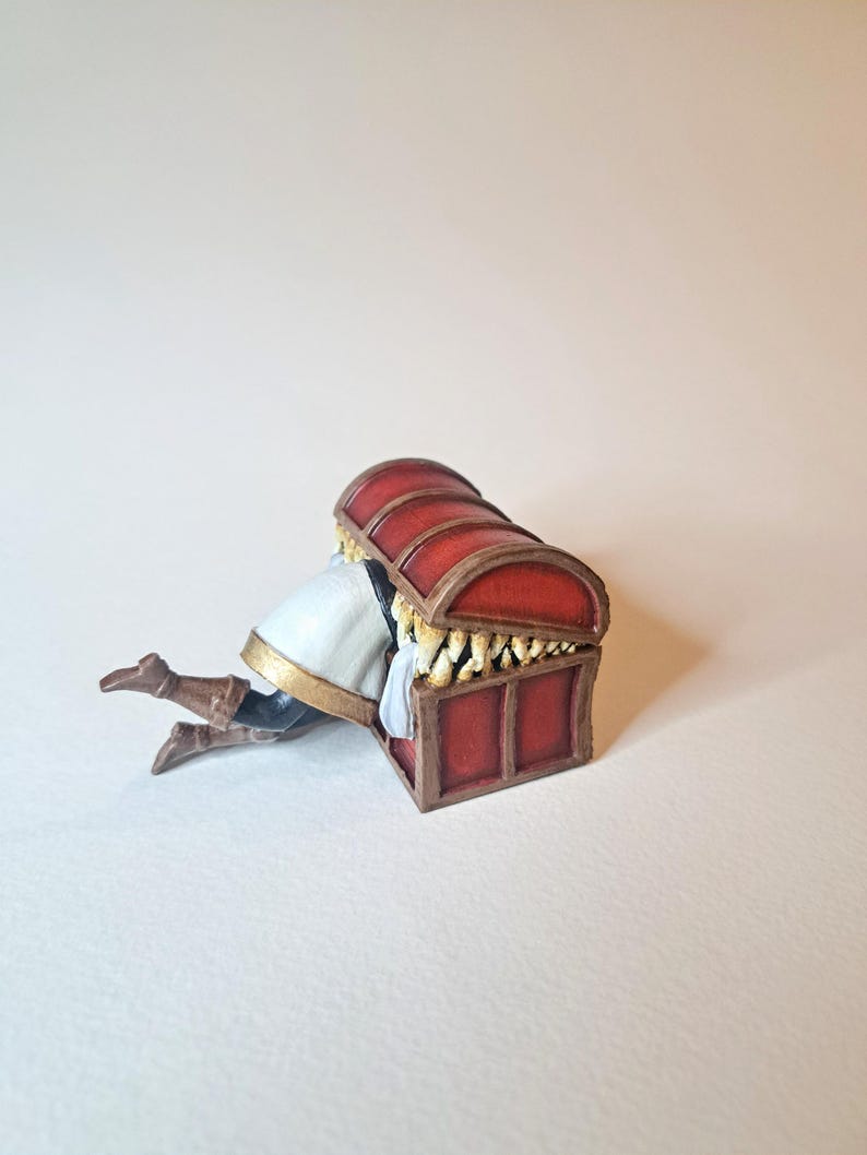 May include: A red wooden treasure chest with gold accents and a white fabric lining. A miniature figure is hiding inside the chest.