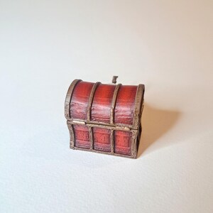 May include: A small, wooden treasure chest with a hinged lid and metal accents. The chest is painted red with brown wood grain details.