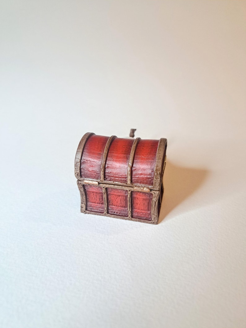 May include: A small, wooden treasure chest with a hinged lid and metal accents. The chest is painted red with brown wood grain details.