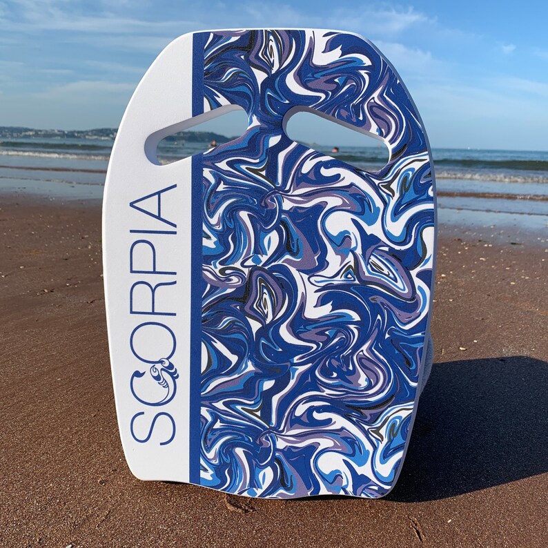 May include: A white and blue bodyboard with a handle cutout. The board features a swirling pattern in shades of blue, white, and gray. The word "SCORPIA" is printed vertically in blue on the left side of the board.