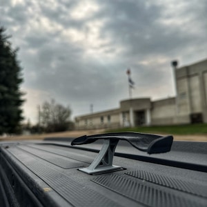 Peut inclure: Un aileron de voiture noir et gris monté à l'arrière d'une voiture noire. L'aileron est en plastique et présente un design élégant et aérodynamique.