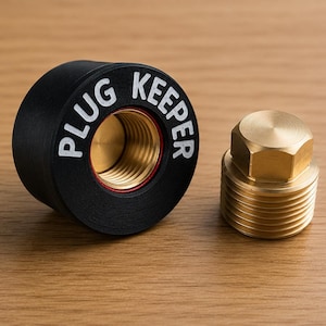 May include: A black cylindrical Plug Keeper with white text and a brass-coloured threaded interior, positioned next to a separate brass-coloured threaded plug with a hexagonal top. The components feature metallic and matte black finishes.