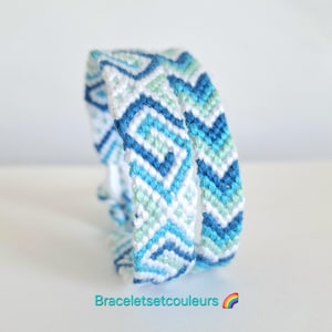 Op de afbeelding: Twee handgemaakte vriendschapsarmbanden met een geometrisch patroon in tinten blauw, wit en lichtgroen. De armbanden zijn gemaakt van geweven draad en worden gepresenteerd op een wit oppervlak. De tekst "Braceletsetcouleurs" is onderaan zichtbaar.