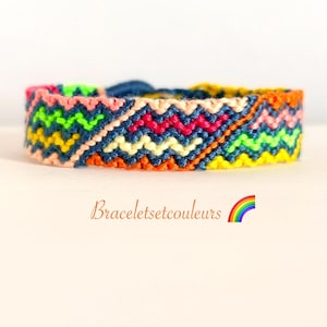 Op de afbeelding: Een kleurrijke geweven armband met een zigzagpatroon in roze, groen, geel, oranje en blauw. De tekst "Braceletsetcouleurs" staat eronder, met een regenboogafbeelding.