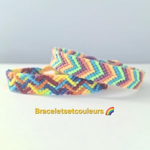 Op de afbeelding: Twee kleurrijke vriendschapsarmbanden met zigzagpatroon. De armbanden hebben een mix van regenboogkleuren, waaronder blauw, geel, oranje, paars en groen. De tekst "Braceletsetcouleurs" wordt in het geel weergegeven.