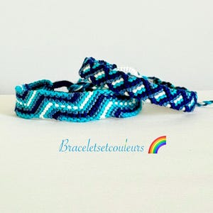 Op de afbeelding: Drie handgemaakte vriendschapsarmbanden in blauw- en wittinten. De armbanden hebben zigzagpatronen en zijn op elkaar gestapeld. De tekst "Braceletsetcouleurs" is zichtbaar met een regenboogafbeelding.