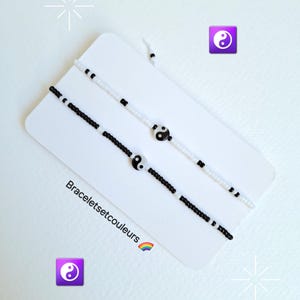 Peut inclure: Deux bracelets en perles noires et blanches avec un charme yin yang sur chacun. Les bracelets sont sur un fond blanc avec le texte "Braceletsetcouleurs" et un emoji arc-en-ciel.