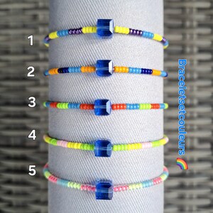 Peut inclure: Cinq bracelets en perles colorées avec des breloques carrées bleues. Les bracelets sont numérotés de 1 à 5. Le texte "Braceletsetcouleurs" est visible sur le côté droit de l'image.