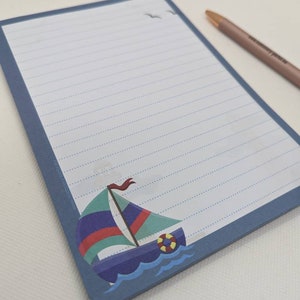 May include: A blue notepad with lined paper and a sailboat illustration. The sailboat is blue, green, red, and yellow. The notepad has a blue border.