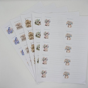 Könnte beinhalten: Ein Stapel weißer Adressetiketten mit dekorativen Aquarellillustrationen. Designs umfassen einen blauen Vogel, eine Schreibmaschine, ein Haus, Bücher und einen Briefkasten. Jedes Etikett hat den Text "Please deliver to".