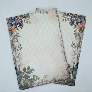 Op de afbeelding: Twee vellen gelijnd briefpapier met een bloemenrand. De rand heeft bloemen in aquarel-stijl in tinten blauw, roze en oranje, samen met groene bladeren en paarse druiven. Het papier heeft een vintage, verouderde uitstraling.